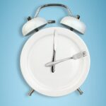 Intermittent fasting concept, food and weight loss plate as a blue alarm clock