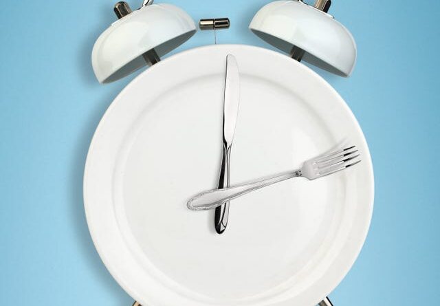 Intermittent fasting concept, food and weight loss plate as a blue alarm clock